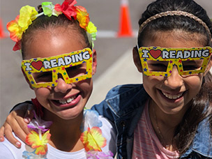 Two girls wearning cardboard I Love Reading glasses